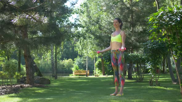 Sporty Woman with Dumbbells Flexing Muscles Outdoors