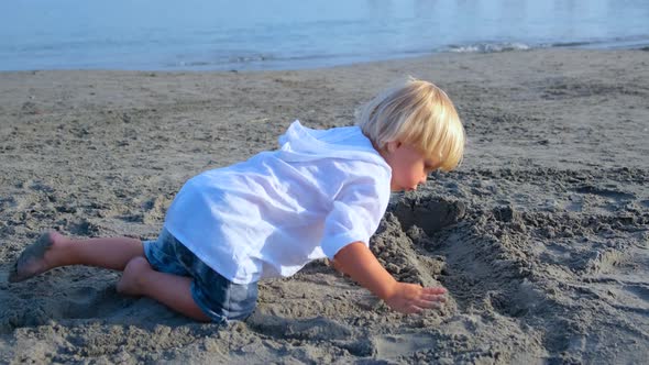 Little Boy in a White Shirt Plays in the Sand on the Beach