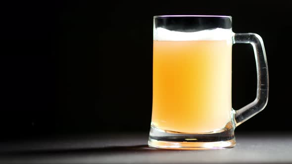 Big Glass Mug Full of Beer with Foam Slowly Rotating Isolated at Black Studio Background