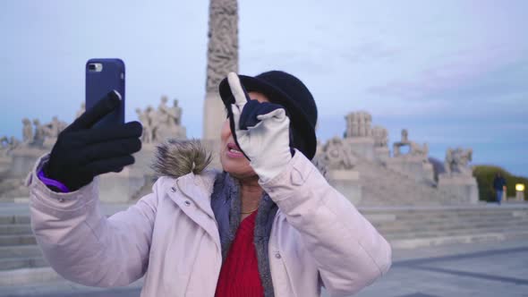 Asian woman standing and taking video call in public Frogner park, Norway