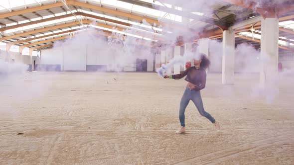 Female dancer in an empty warehouse holding smoke grenade