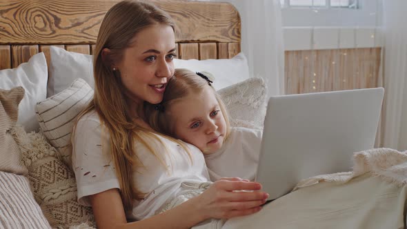 Young Single Mother Adult Mom Lies in Cozy Bed with Little Girl Daughter Child in Morning in Evening