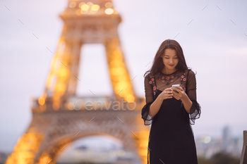 Travel woman using smartphone near the Eiffel tower and carousel, Paris. Evening little noisy image