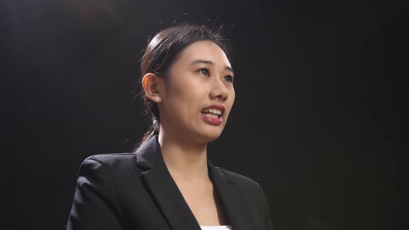 Side View Of Asian Speaker Woman In Business Suit Holding Her Hands Together While Speaking On Stage