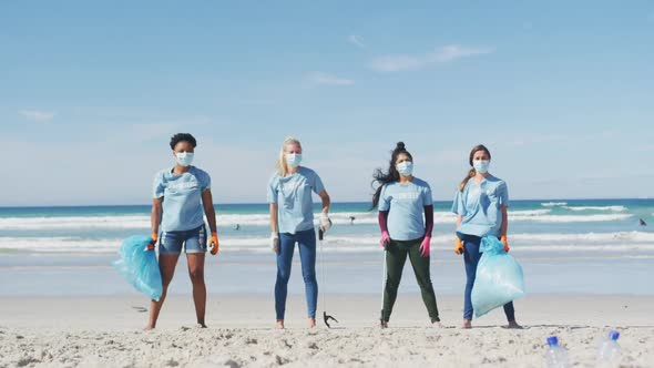 Diverse group of women wearing volunteer t shirts and face masks picking up rubbish from beach