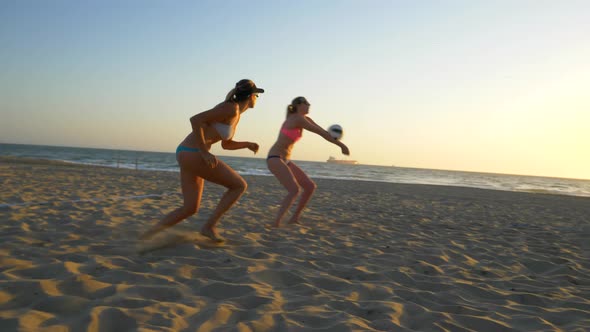 Women players play beach volleyball at sunset and a player hand sets the ball.