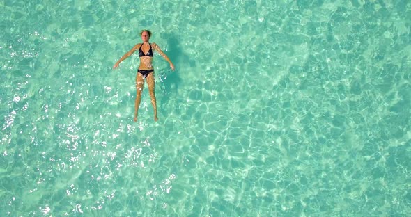 Aerial drone view of a woman floating and swimming on a tropical island.