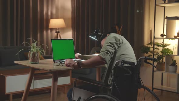 Tried Asian Man Sitting In A Wheelchair Sleep While Working On Green Screen Laptop At Home