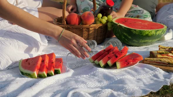 Woman Takes Slice of Watermelon on Blanket at Family Picnic