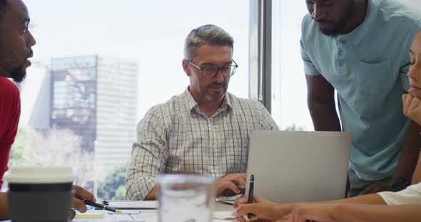 Diverse male and female business colleagues talking and using laptop