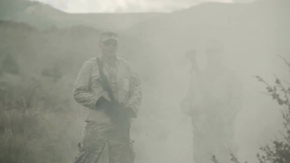 Two soldiers standing in a dissipating cloud of smoke. alt