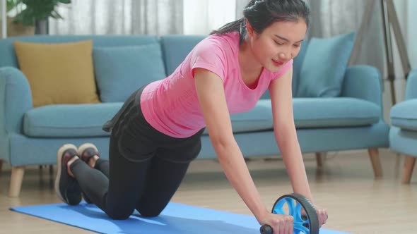 Asian Woman In Sportswear Is Working Out With Exercise Wheel At Home In The Living Room