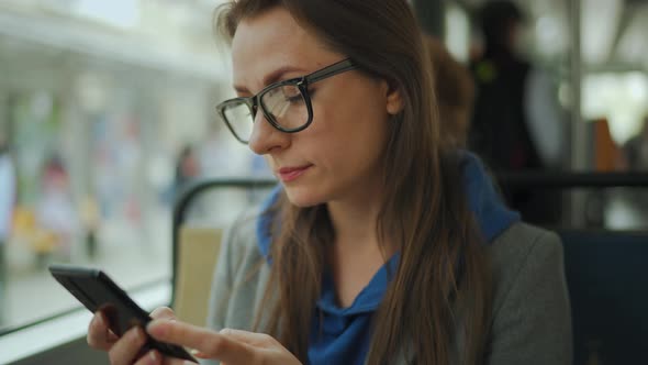 Woman with Glasses in Tram Using Smartphone Chatting and Texting with Friends