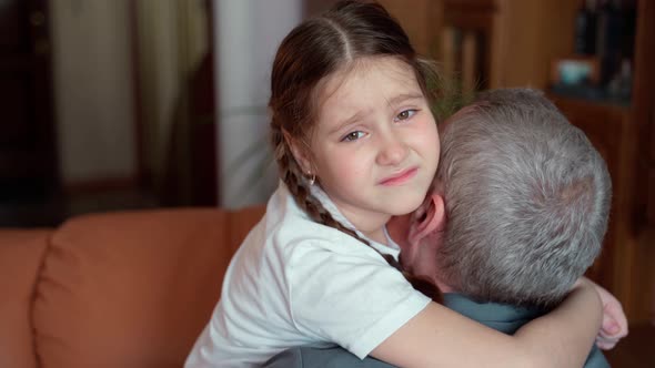 A young girl hugs an elderly 60s unrecognizable grandfather. The girl tries to smile, but she is sad