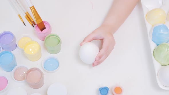 A Little Girl Painting an Egg with Easter Eggs on a White Background Top View