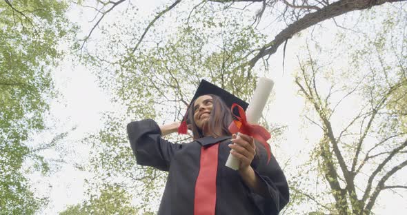 Cheerful Young Lady Putting Off Mortarboard Throwing Up Jumping Outdoors in Park