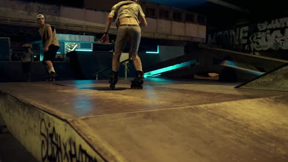 Active Hipsters Performing Jump Trick on Ramp at Night Skate Park with Graffiti