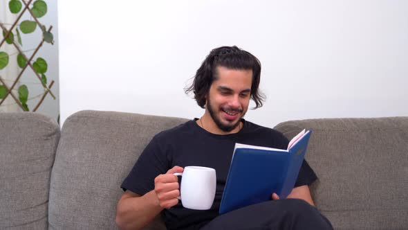 Indian man peacefully reading a book and enjoying coffee