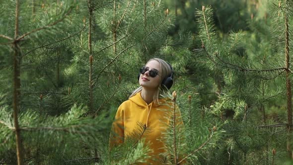 Stylish girl in hoodie listen music in headphones in pine tree forest