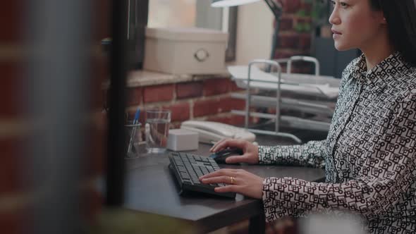 Asian Woman Looking at Monitor to Work on Business Project