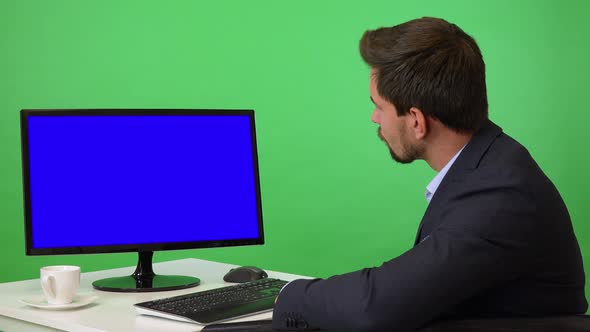 A Young Businessman Sits in Front of a Computer and Looks Seriously at the Camera - Green Screen