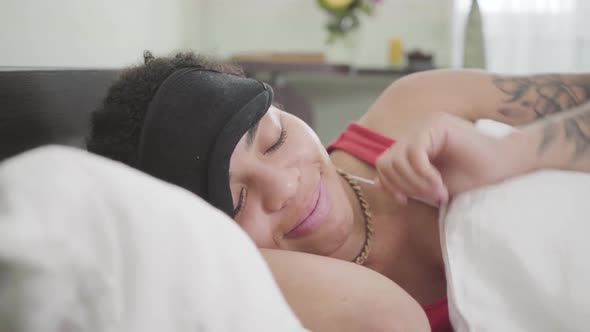 Close-up View of Adorable African American Woman Lying Under White Blanket with Black Sleeping Mask