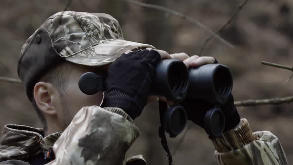 Portrait of Hunter Looks Through Binoculars. Man in Comfortable Camouflage Clothes Hunter Outdoor in