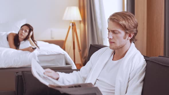 Young Confident Handsome Caucasian Male Sitting at Sofa Reading Morning Newspaper While His