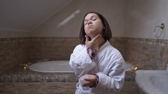 Confident Little Woman Applying Moisturizer on Neck Skin Standing in Bathroom Indoors