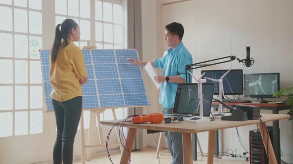 Asian Man And Woman Discuss Work With Solar Cell Panel And Laptop Computer Showing Wind Turbine