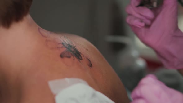 World tattoo day. Tattoo-artist makes a tattoo to client's back and swipes with napkin.