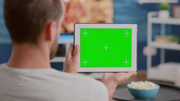 Closeup of Man Holding Digital Tablet with Green Screen Watching Webinar Sitting on Sofa