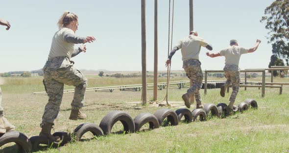 Diverse group ale soldiers running on car tyres at army obstacle course in the sun