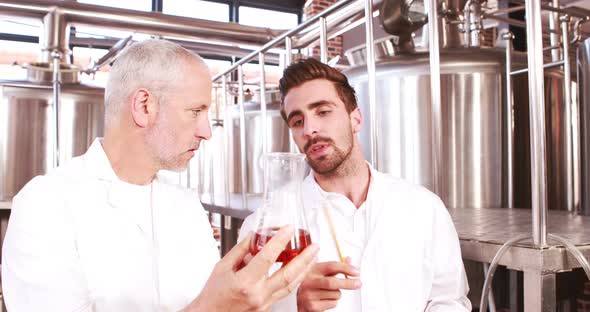 Two men in lab coat looking at the beaker with beer