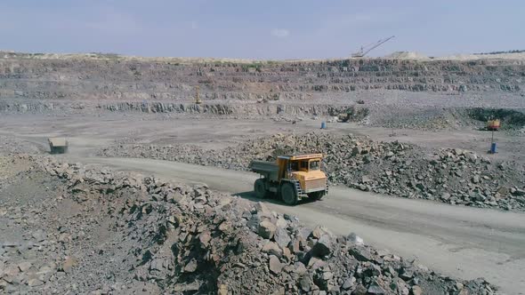Mining Dump Trucks in Large Granite Open Pit Mine. Loaded Truck Rides on Road Quarry Ledge Aerial