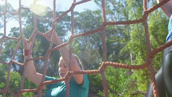 Determined women climbing a net during obstacle course