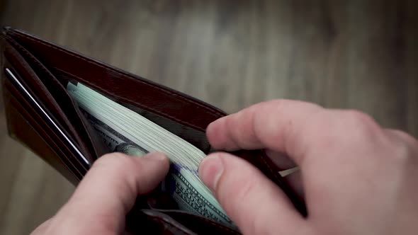 The man's hands open a wallet filled with $ 100 bills and give half of the stack to someone.