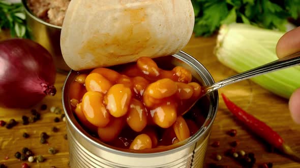 Chef Takes with Spoon Stewed Beans in Tomato Sauce From Metal Tin Can on Wooden Kitchen Board