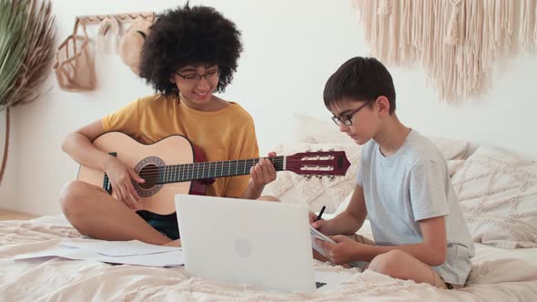 African American Woman Teaches Boy to Play Guitar Using Laptop