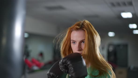 Closeup of Motivated Redhead Sportswoman Boxing Punching Bag in Gym