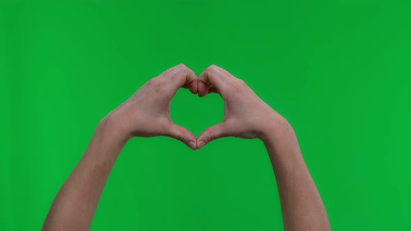 Closeup of a Woman's Hand Shows a Heart Sign on a Green Background