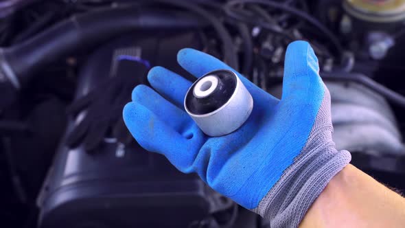 master in glove holds lever silent block in his hand against background engine.