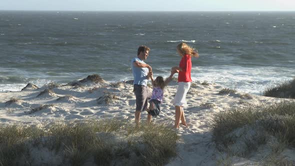 LS Tracking Left OF A MOTHER AND FATHER SWINGING THEIR DAUGHTER IN THE AIR