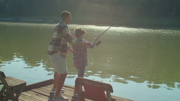 Caring African American Dad Teaching Cute Son to Fish with Fishing Rod on Lake