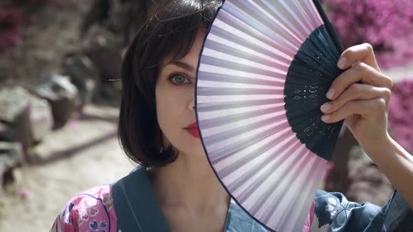 Closeup of Caucasian Geisha Woman in Traditional Japanese Kimono is Covering Her Face with Wooden