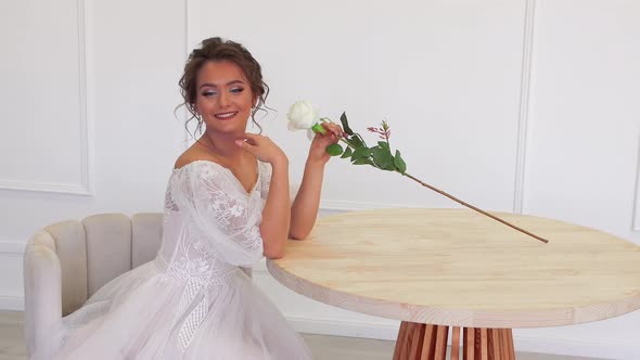 Beautiful Girl Sitting at the Table with a Rose in Her Hand Posing