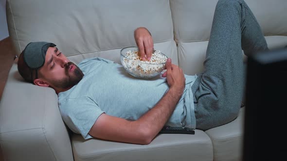 Tired Man Relaxing on Sofa in Front of Television Eating Popcorn While Watching Movie Show