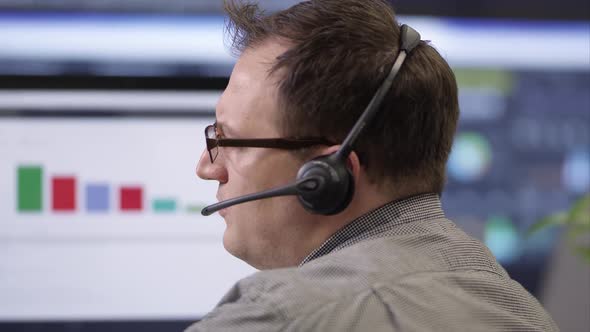 Side view of man talking on headset in front of computer.