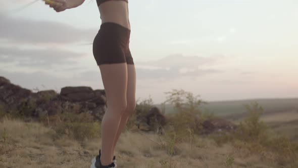 Woman in Sports Top Trains with Rope in Nature Camera Moves From the Bottom Up Side View