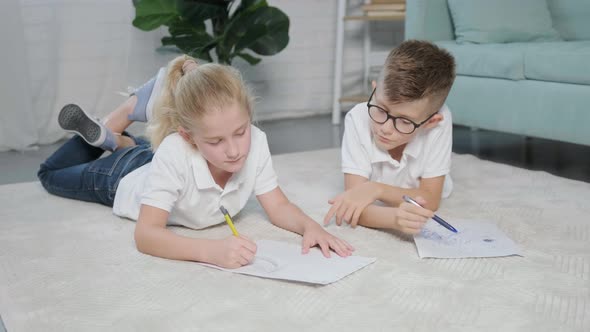 Portrait of Twins Girl and Boy Drawing While Lying on the Floor at Home